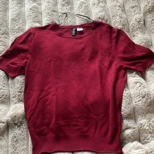 Mörkröd stickad tröja från H&M - En enkel och stilren mörkröd stickad tröja från H&M. Tröjan har korta ärmar, rund halsringning och ribbade kanter. Perfekt för dig som gillar en klassisk look med en pop av färg.