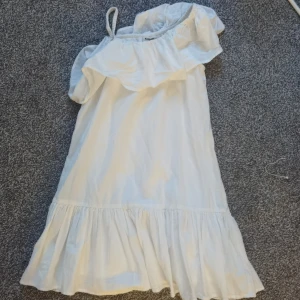 Vit offshoulder klänning Kappahl 140 - Superfin vit kortklänning från Kappahl i bomull. Klänningen har offshoulder-design med volang upptill och en axelrem, samt en volangkant nertill. Har använts 3 gånger så nästan i helt nytt skick och inte de minsta tecken på användning 💓