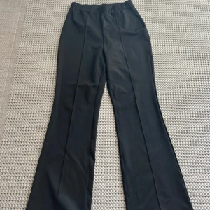 Svarta utsvängda byxor från SHEIN L - Svarta utsvängda byxor från SHEIN i storlek L. Byxorna har hög midja, raka pressveck och en snygg bootcut passform. Tillverkade i ett mjukt och lätt syntetmaterial som ger en clean look. Perfekta till en trendig outfit.