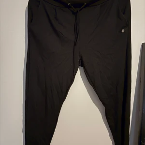 Svarta mjukisbyxor från Zink - Svarta mjukisbyxor från Zink med dragsko i midjan och fickor på sidorna. Sköna och enkla att styla, perfekta för chill dagar. Materialet är mjukt och stretchigt, vilket gör dem riktigt bekväma att ha på sig.