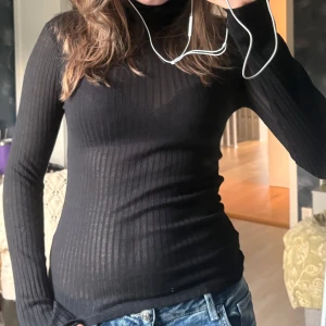 Svart ribbad polotröja i stretch - Svart långärmad polotröja med ribbat mönster och tight passform. Tredje bilden är ganska lik fast utan polo, aldrig använt