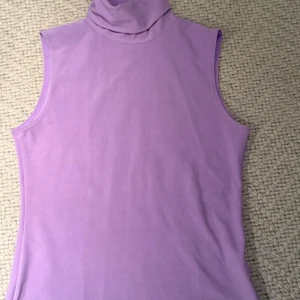 Syrenlila polotopp från Cami Team strl M - Säljer en lila ärmlös polotopp från Cami Team i mjukt material. Toppen har hög krage och en clean, enkel design som är lätt att styla. Perfekt för dig som gillar färg och vill ha något bekvämt och snyggt.