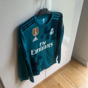 Real Madrid bortaställ 2018 - Säljer en långärmad Real Madrid bortatröja från Adidas med Ronaldo 7 på ryggen.  pixelmönster. Officiella klubbmärken, Champions League-märke på ärmen och Fly Emirates-logga. Liten defekt på vänster arm/ axel. Inget som syns vid användning men kan bli till dessvärre större hål om man ej tar hand om! Autentisk/ äkta! Mvh ItsForfits 🌟