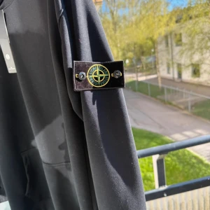 Svart hoodie från Stone Island L - Svart hoodie från Stone Island i storlek L. Klassisk modell med huva, känguruficka och ikonisk logga på vänster ärm. Tröjan har lång ärm och är tillverkad i mjuk bomull, perfekt för en clean och stilren look.