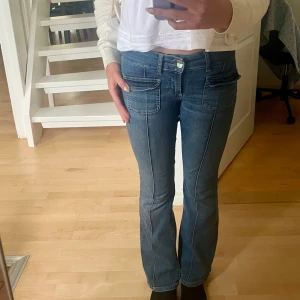 Blå bootcut jeans med fickor - Snygga blå jeans med bootcut-modell och stora fickor framtill. Jeansen har en låg midja och markerade sömmar längs benen. Dessa jeans är också av ett stretchigt material. Perfekta för dig som gillar en klassisk men ändå trendig look.