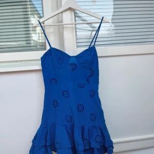 Blå klänning från Zara - Supersöt blå klänning från Zara med smala axelband och volangkant nertill. Klänningen har broderade blommor och är gjord i bomull, perfekt för varma dagar. Sitter snyggt med smock i ryggen och har en feminin, luftig känsla. En broderad blomma har en lös tråd 💕