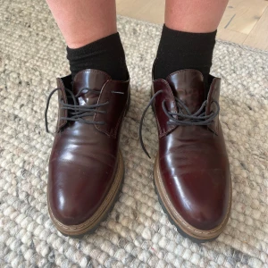 Vinröda chunky loafers i skinn - Snygga vinröda loafers köpta i Italien med chunky sula och snörning. Skorna har en rund tå och är tillverkade i glansigt skinn med kontrasterande brun sula och svart yttersula.