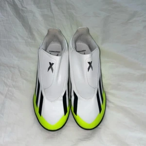 Adidas X Crazyfast4 fotbollsskor vit/gul - Säljer ett par Adidas X Crazyfast4 fotbollsskor i vitt med neongula och svarta detaljer. Skorna har en slimmad form, täckt snörning med kardborre och greppig svart sula för konstgräs. Perfekta för dig som vill sticka ut på planen.