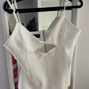 Vit korsettopp med rosetter och dragkedja - Supersnygg vit korsettopp från Bershka med dubbla smala axelband, två söta rosetter framtill och dragkedja i ryggen. Toppen har en figurnära passform och stilren design som ger en modern och chic vibe. Toppen ör i storlek L men väldigt liten i modellen, passar mug som annars har s i toppar