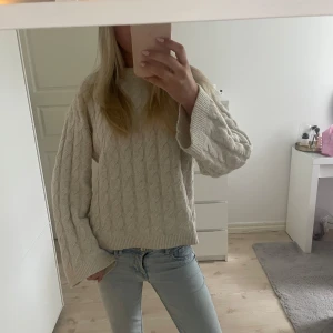 Beige kabelstickad tröja från H&M - Supermysig beige kabelstickad tröja från H&M i storlek XS. Tröjan har breda ärmar och klassisk rund halsringning. Perfekt för lager-på-lager och chill dagar. Snygg till både jeans och kjol, och den stickade strukturen ger en extra cozy vibe. Passar även S