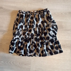 Leopardmönstrad volangkjol Pernilla Wahlgren - Säljer en kort kjol från Pernilla Wahlgren med leopardmönster i svart, beige och brunt. Kjolen har volangdetaljer och omlottkänsla, perfekt för dig som gillar att sticka ut. Resår i midjan för skön passform.