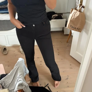 Svarta bootcut jeans  - Säljer ett par svarta jeans med bootcut passform. Byxorna har klassisk femficksdesign, silverfärgade knappar och en snygg, något utsvängd benvidd. Perfekta för dig som gillar en tidlös och clean look. Storlek medium längd 33