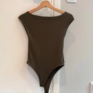 Mörkgrön body från Zara - Säljer en grön body från Zara med ärmlös design. Tight passform som lägger sig efter kroppen.
