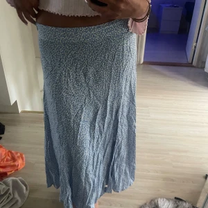 Blommig blå långkjol från H&M - Supersöt långkjol från H&M i ljusblått med små vita och gula blommor över hela tyget. Kjolen har en flowy passform och är gjord i mjuk bomull, perfekt för varma dagar. Sitter snyggt i midjan och ger en chill och somrig vibe. Strl 42 men jag har vanligtvis 34-36
