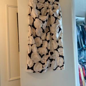 Beige och svart omlottkjol från H&M - Snygg lång omlottkjol från H&M i linnemix med beige och svart mönster som påminner om snäckor. Kjolen har knytning i midjan och en avslappnad passform, perfekt för varma dagar. Materialet är luftigt och känns fräscht mot huden.