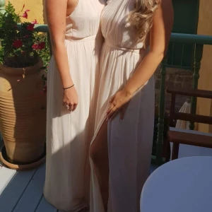 Ljus maxiklänning med öppen rygg - Elegant maxiklänning i chiffong med plisserad överdel, markerad midja & smala axelband dekorerade med strass. Klänningen har öppen rygg med diskret knäppning i nacken samt en dold dragkedja i sidan, & en hög slits framtill. Färg ljusrosa/nude. Storlek S. Endast använt en gång. Mycket fint skick.