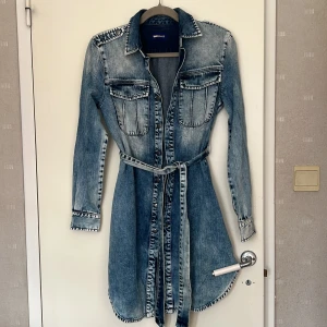 Jeansklänning/ lång jeans jacka med bälte från GAS - Snygg jeansklänning från GAS med knappar framtill, långa ärmar och två bröstfickor. Klänningen har ett avtagbart bälte i midjan. Perfekt för dig som gillar denim och vill ha en avslappnad men trendig look. Aldrig använt, är i helt nyskick!!