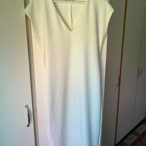 Vit långklänning med v-ringning - En stilren vit långklänning med v-ringad hals och minimalistisk design. Klänningen har korta ärmar och rak passform, perfekt för dig som gillar en clean och elegant look.