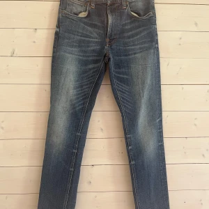 Blå jeans från Nudie Jeansco W29 L32 - Säljer ett par klassiska blå jeans från Nudie Jeansco med snygga slitningar och kontrastsömmar. Modellen har raka ben och normal passform. Bakfickorna har Nudie Jeans typiska broderi. Perfekta för en avslappnad och stilren look. OBS är upplagda vid frågor om mått kontakta mig! 