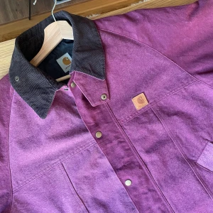 Carhartt jacka - Snygg vinröd jacka från Carhartt med kontrasterande mörk krage i manchester. Jackan har knappar framtill, två snedställda fickor och klassisk Carhartt-logga på bröstet. Perfekt för dig som gillar streetwear och vill ha en stilren look. Storleken är XXL men jag skulle säga motsvarar svensk L.