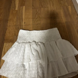 Vit volangkjol med smock i midjan - Supersöt vit kortkjol med bred smock i midjan och dubbla volanger. 