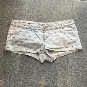 Vita mönstrade low waist  jeansshorts - Snygga vita jeansshorts med grått prickigt mönster och klassisk femficksdesign. De har låg midja, bälteshällor och knappstängning framtill. Perfekta för varma sommardagar och ger en fräsch look till din outfit. De är lite för stora till mig i midjan så de referens på några andra artiklar jag säljer!💕💕