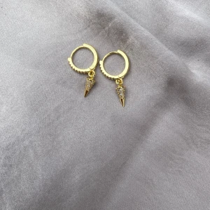 Guldiga örhängen med strass och spikes - Snygga guldiga hoops med små glittriga strass och spetsiga spikes som hänge. Perfekta för dig som vill ha en edgy men ändå glam look. Runda ringar med cool detalj, passar till alla outfits.