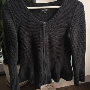 Svart stickad kofta från Chelsea - Svart stickad kofta från Chelsea i storlek M. Koftan har grovstickad struktur, långa ärmar och dragkedja framtill. 