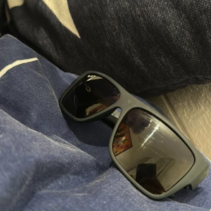 Svarta Ray-Ban solglasögon RB1542 (Samma som Bruce Lee har) - Snygga svarta Ray-Ban solglasögon, modell RB1542, med breda skalmar och klassisk fyrkantig form. Tillverkade i Italien med diskret Ray-Ban-logo i silver på sidan. Perfekta för dig som vill ha en stilren och cool look.