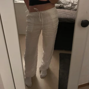 Lågmidjade linnebyxor - Säljer ett par vita linnebyxor med avslappnad passform och snörning i midjan. Byxorna är raka i modellen och perfekta för en chill och stilren look. Lätta och luftiga, perfekta för varmare dagar.