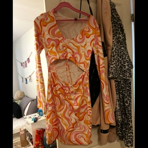 Färgglad cut out klänning H&M Divided - Säljer en kort klänning från H&M Divided med färgglatt psykedeliskt mönster i rosa, orange, gul och vit. Klänningen har lång ärm, cut out-detalj vid midjan och rynk framtill! Använd 2 gånger och köpt för 3 år sen men aldrig haft så mycket  användning av den och nu är den förliten.