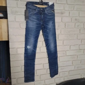 Replay Anbass slim jeans blå - Snygga Replay Anbass jeans i blå tvätt med slitningar och slim passform. Klassisk femficksmodell med dragkedja och detaljerade bakfickor. Jeansen har en fräsch, modern look och är tillverkade i stretchig bomullsdenim för extra komfort.
