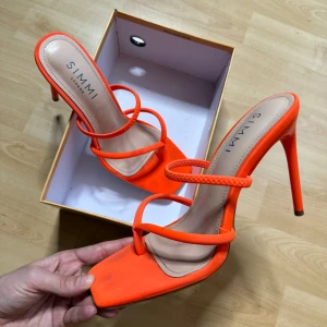 Orange klackpumps från Simmi London - Snygga orange pumps med hög klack från Simmi London. Skorna har fyrkantig tå, tunna remmar och öppen tå. Perfekta för att sticka ut med en färgstark look. Tillverkade i syntetmaterial med en stilren design. Org pris: 500kr. 