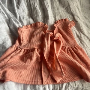 Persikofärgad volangig tubtopp - Supersöt persikofärgad tubtopp med volangkant upptill och knytning i ryggen. Passar mig som har xs-S i toppar!!