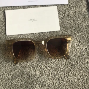 Beige solglasögon från CHIMI - Snygga solglasögon från CHIMI i modellen 04 ECRU. De har en fyrkantig form med transparent beige båge och bruna tonade glas. Perfekt accessoar för att lyfta din stil. Dom är lite nötta runt örat som ni ser på sista bilden. Dom är så gott som splitter nya annars allt följer med även putsduken! Priset går att diskutera vid snabb affär! Skriv vid minsta fundering.
