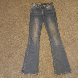 Blå bootcut jeans med broderade bakfickor - Säljer ett par blå bootcut jeans med snygga broderade detaljer och knappar på bakfickorna. Jeansen har klassisk femficksdesign och lätt slitning framtill. Perfekta för dig som gillar en lite vidare passform nertill.
