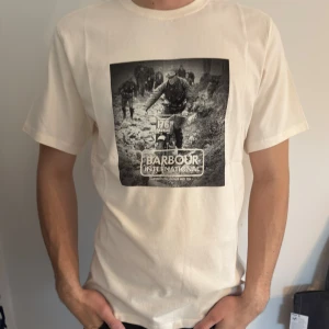 Vit t-shirt ifrån Barbour International - Säljer en vit t-shirt från Barbour International med ett svartvitt tryck av en motorcyklist på bröstet. T-shirten har rund hals och normal passform. Perfekt för dig som gillar stilrena T-shirts