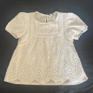 Vit blus med broderade detaljer - Vit blus med korta puffärmar och  broderade hålmönster. Strl S