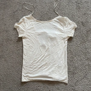 Vit croppad topp med rosett i ryggen - Säljer en vit croppad topp med smala axelband och öppen rygg med en snygg rosettdetalj. Toppen är i ett mjukt material och har en enkel, stilren design som passar perfekt till sommaren.