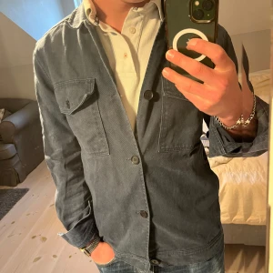 Blå overshirt från These Glory Days - Säljer en stilren marinblå overshirt från These Glory Days i storlek S. Jackan har knäppning framtill, två bröstfickor och två gömda fickor vid sömmen. Tjockare material liknande denim. Mycket fint skick utan defekter.