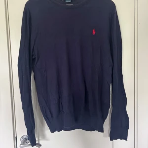 Mörkblå tröja från Ralph Lauren - Mörkblå långärmad tröja från Ralph Lauren med den klassiska röda loggan broderad på bröstet. En skit snygg tröja för sommaren. Lätt i materialet så de blir inte för varmt och den är lätt att matcha med. Säljer den för de ligger bara i min garderob och skräpar. Jag inte använt jätte mycket. De är bara hojta till för fler bilder. Pris går att diskutera 