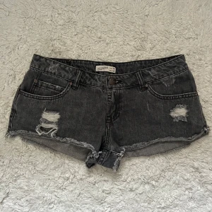 Lågmidjade jeansshorts - Snygga grå jeansshorts med slitna detaljer och råa kanter. Klassisk femficksmodell med knapp och dragkedja framtill. Perfekta för varma dagar och en avslappnad stil. 