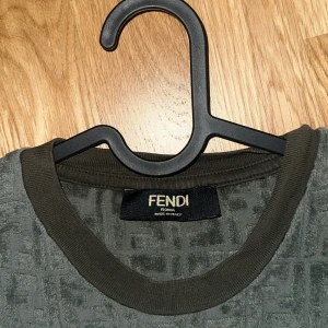 Fendi tröja - Säljer en mörk grön t-shirt från Fendi med heltryckt FF-mönster. T-shirten har rund halsringning och korta ärmar. Perfekt för dig som gillar exklusiva märken och stilren design.