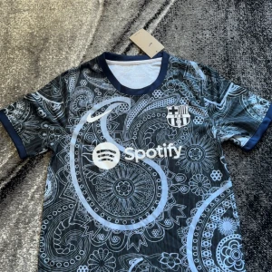 Barcelona fotbollströja - Säljer en Barcelona fotbollströja med Spotify-logga och paisleymönster i vitt och ljusblått på svart botten. Tröjan har korta ärmar och rund halsringning med mörkblå kant. Perfekt för dig som vill sticka ut på planen eller läktaren.