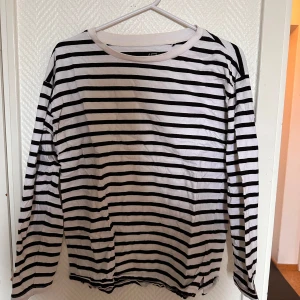 Randig långärmad tröja från 157 - Säljer en klassisk vit och svart randig långärmad tröja från 157. Tröjan är tillverkad i 100% bomull och har en rund halsringning. Perfekt för en avslappnad och stilren look.