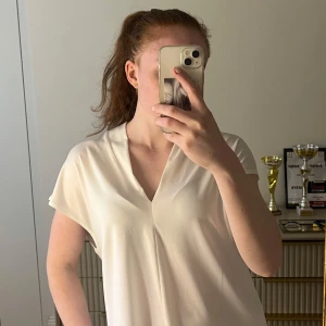 Vit blus med v-ringning - Säljer en stilren vit blus med v-ringning och korta ärmar. Blusen har en lös passform och är perfekt för sommaren. Passar till många olika outfits och är lätt att matcha. 