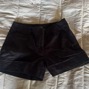 Svarta shorts från H&M - Svarta shorts från H&M med klassisk design och uppvikta benslut. De har fickor både fram och bak samt hällor för skärp. Perfekta för varma dagar och enkla att matcha med olika toppar.