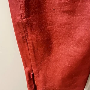 Röda skinnbyxor från Conleys Black - Snygga röda skinnbyxor från Conleys Black med klassisk femficksdesign och knappstängning framtill. Byxorna har raka ben och en stilren look som sticker ut. Perfekta för dig som vill ha något unikt i garderoben.