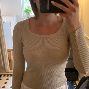 Beige ribbad långärmad topp - Säljer en beige ribbad långärmad topp med rund halsringning. Sitter tight och är perfekt att styla till både jeans och kjol. Mjuk och stretchig i materialet, superenkel att matcha med andra plagg.