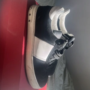 Valentino flycrew  - Snygga svarta och vita sneakers från Valentino med klassisk design. Skorna har svarta snören, vit hälkappa och dekorativa nitar på baksidan av sulan. Perfekta för dig som gillar stilrena och exklusiva sneakers. En nit är borta. 36/5 men passar 37 37,5